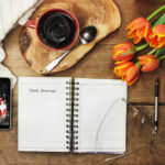 food journal on table with cup of coffee and flowers