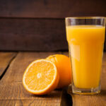 glass of orange juice and fresh orange on wooden table