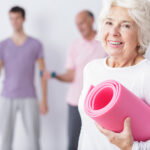 Older woman smiling with yoga mat