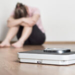 Disappointed woman sitting on floor next to scale