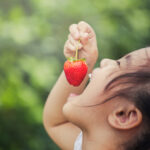 Happy young girl eating a strawberry