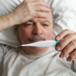 Older man sick in bed taking his temperature