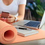 woman with cell phone, laptop, and yoga mat