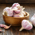 Bulbs of garlic in wooden bowl on table