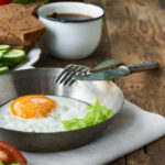 Fried egg in bowl with knife and fork on wooden table