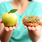 One hand holding an apple the other hand holding a sprinkle doughnut