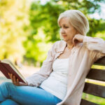 Woman sitting on bench in the park reading a book