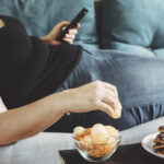 Woman lying on couch eating chips